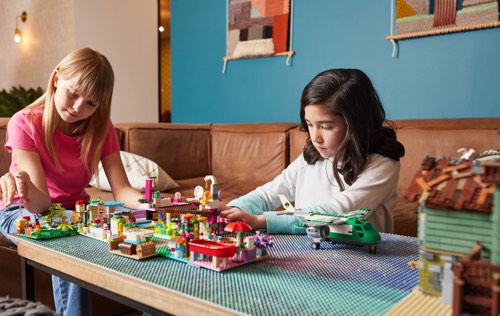Two girls playing with blocks, airplanes, and buildings on Slab Dream Lab custom printed baseplate