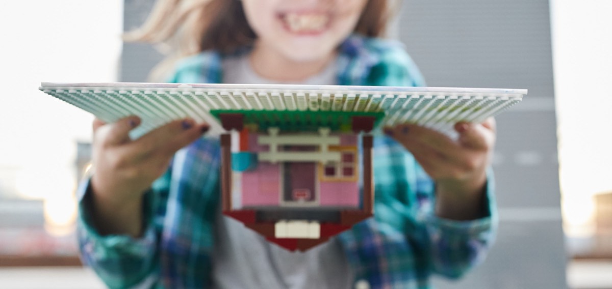 Girl holding slab baseplate upside down with blocks buildings on it, not falling off
